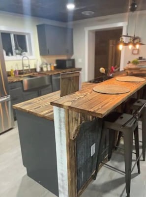 A modern kitchen with a wooden island, dark cabinets, and a hanging light fixture.