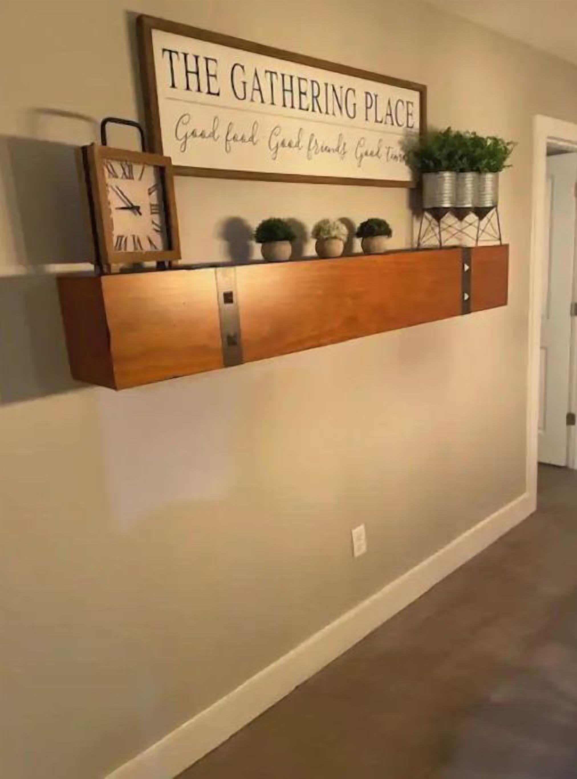 A hallway with a wooden shelf displaying a clock, potted plants, and a sign reading "THE GATHERING PLACE".