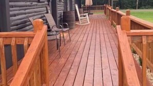 Una terraza de madera que conduce a una cabaña con un porche cubierto, amueblado con sillas y una mesa.