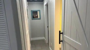 Un pasillo con piso de color claro, una puerta con picaporte negro y un pequeño cuadro en la pared.