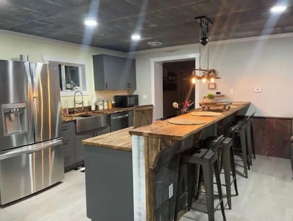 A modern kitchen with stainless steel appliances, a wooden island, and bar stools.