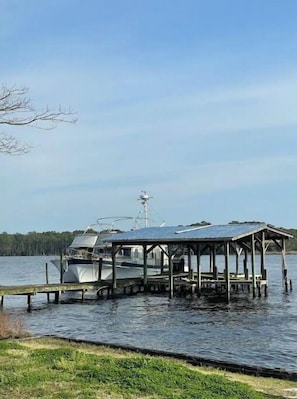 A docked boat with a covered structure, a wooden pier, and a grassy area in the foreground.