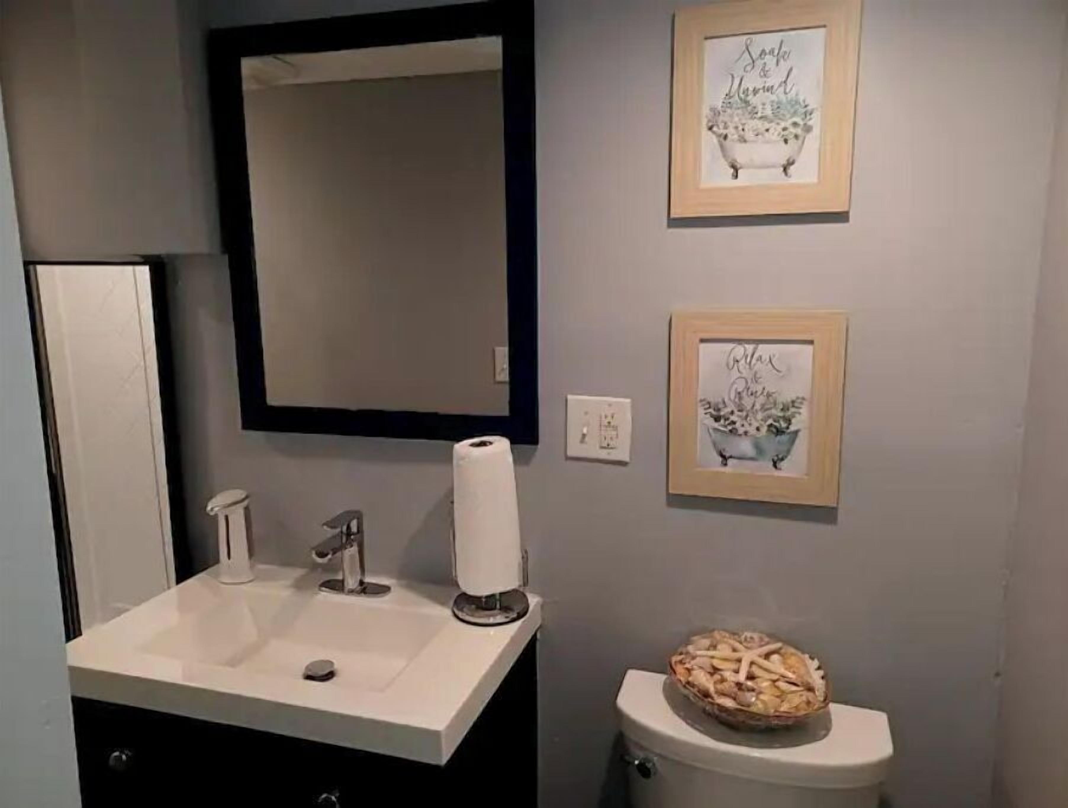 Une salle de bain avec un lavabo blanc, un miroir et deux tableaux encadrés accrochés au mur.