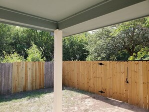 A covered outdoor area with a wooden fence, a concrete pillar, and a view of trees and greenery.