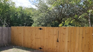 A wooden fence with a gate, a dirt path, and trees in the background. - Sanctuary, Lackland AFB, SeaWorld Fiesta Texas (San Antonio)