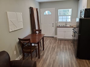 A compact kitchen with a dining area, a refrigerator, and a window with blinds.
