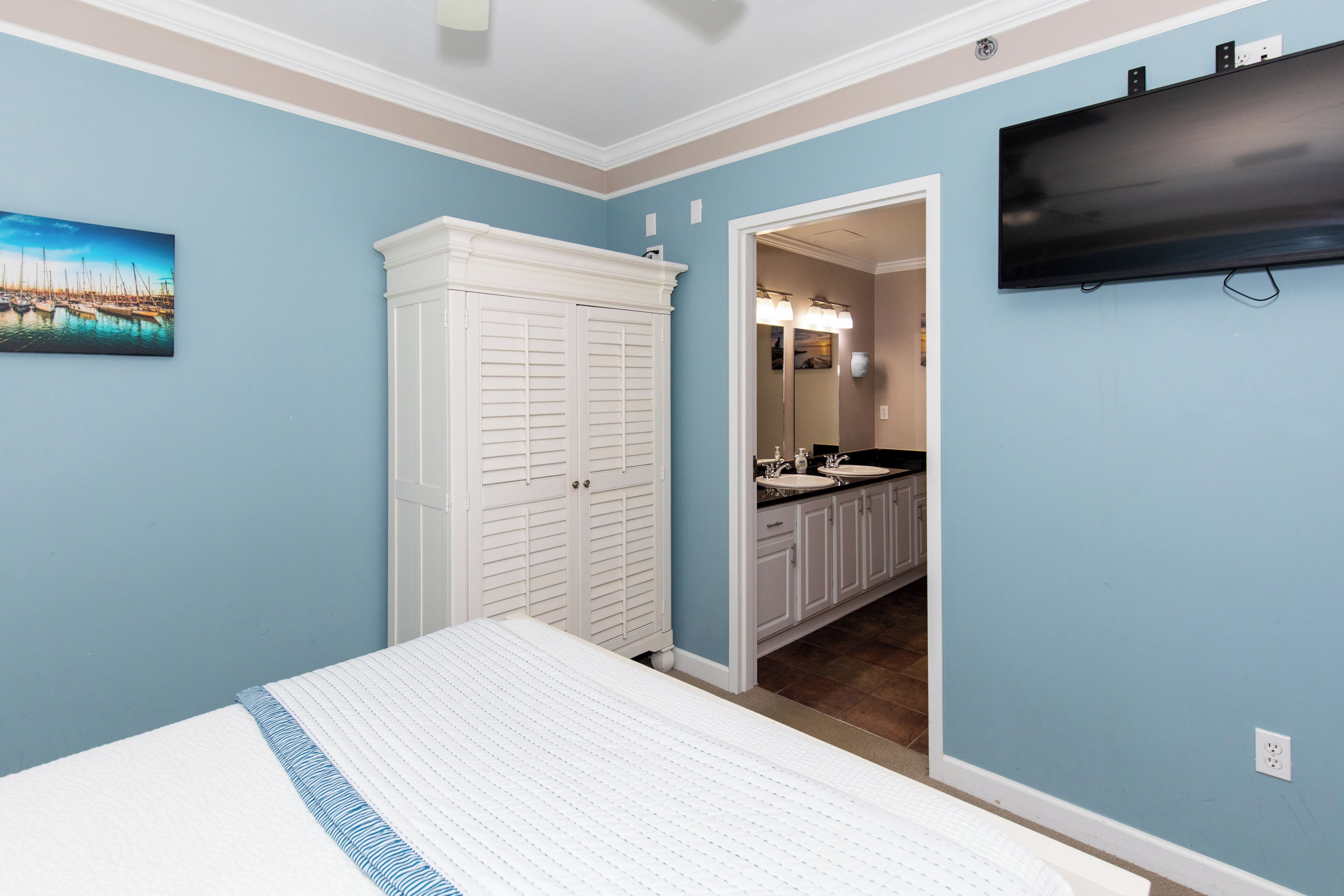 A bedroom with a bed, a white closet, a TV mounted on the wall, and a bathroom visible through an open door.