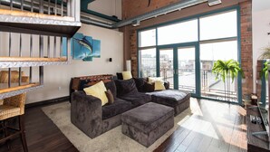 Ein großzügiger Wohnbereich mit einer großen Eckcouch, einem Esstisch mit Stühlen, einem Balkon mit Aussicht und einer Decke mit freiliegenden Lüftungsrohren und einer Haishark-Dekoration.
