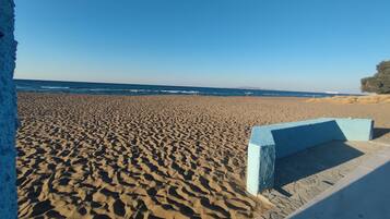 A sandy beach with a clear blue sky and a distant view of the sea.