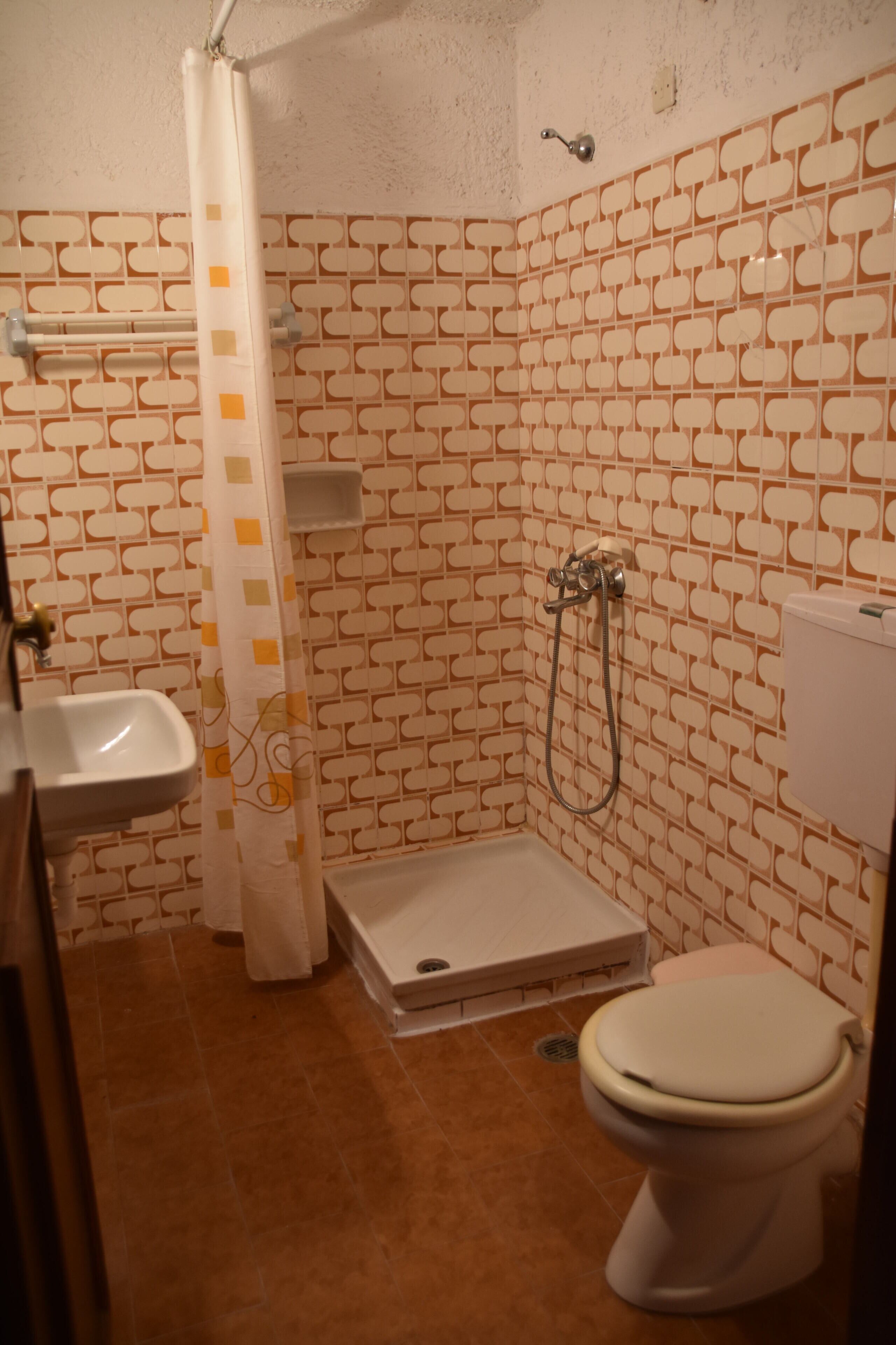 Ein Badezimmer mit Wandfliesen mit Muster, einer Dusche, einer Toilette und einem Waschbecken.