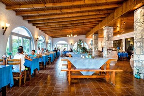 A restaurant with wooden beams, stone pillars, and blue tablecloths. - Hotel Tsagarakis Beach (Malevizi)