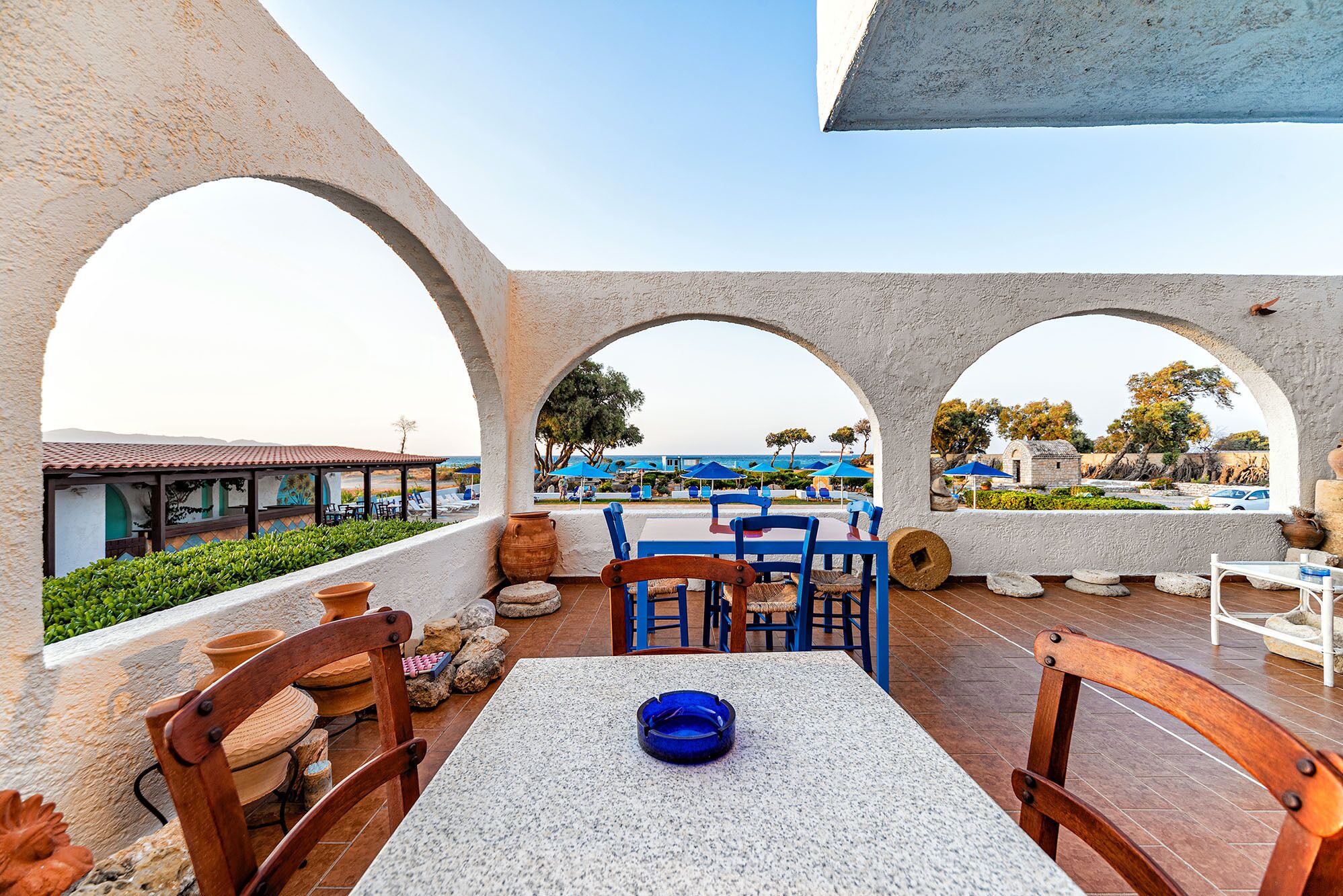 A terrace with a table and chairs, a view of the sea, and a covered area with umbrellas.