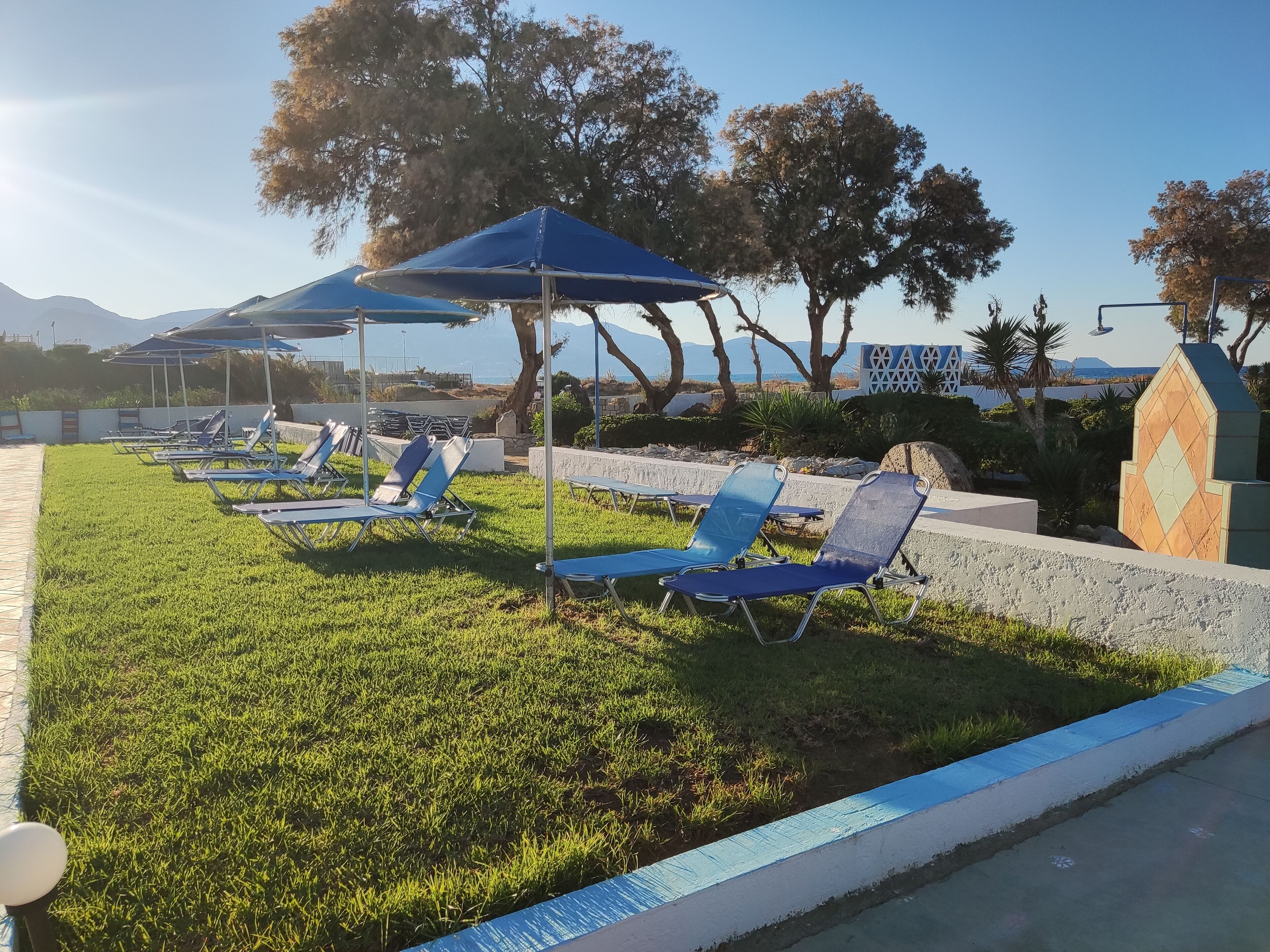 A poolside area with sun loungers and umbrellas, surrounded by trees and a view of mountains.