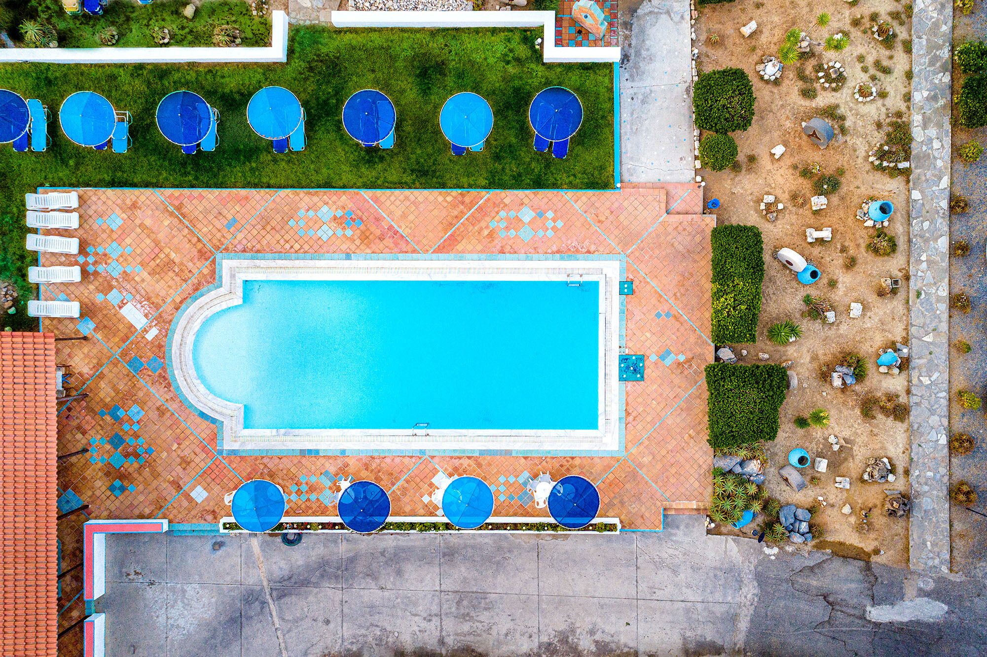 Vue aérienne d’un espace piscine avec une terrasse carrelée, plusieurs chaises longues et un petit jardin agrémenté de rochers et de plantes.