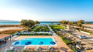 A resort pool area with a view of the sea, lounge chairs, and a small building. - Hotel Tsagarakis Beach (Malevizi)