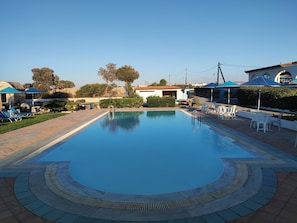 A swimming pool with a tiled deck, lounge chairs, and umbrellas. - Hotel Tsagarakis Beach (Malevizi)