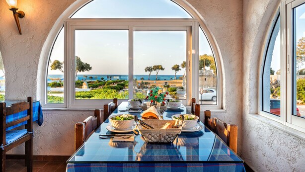 A dining area with a table set for two, overlooking a scenic view of the sea and a landscaped garden. - Hotel Tsagarakis Beach (Malevizi)