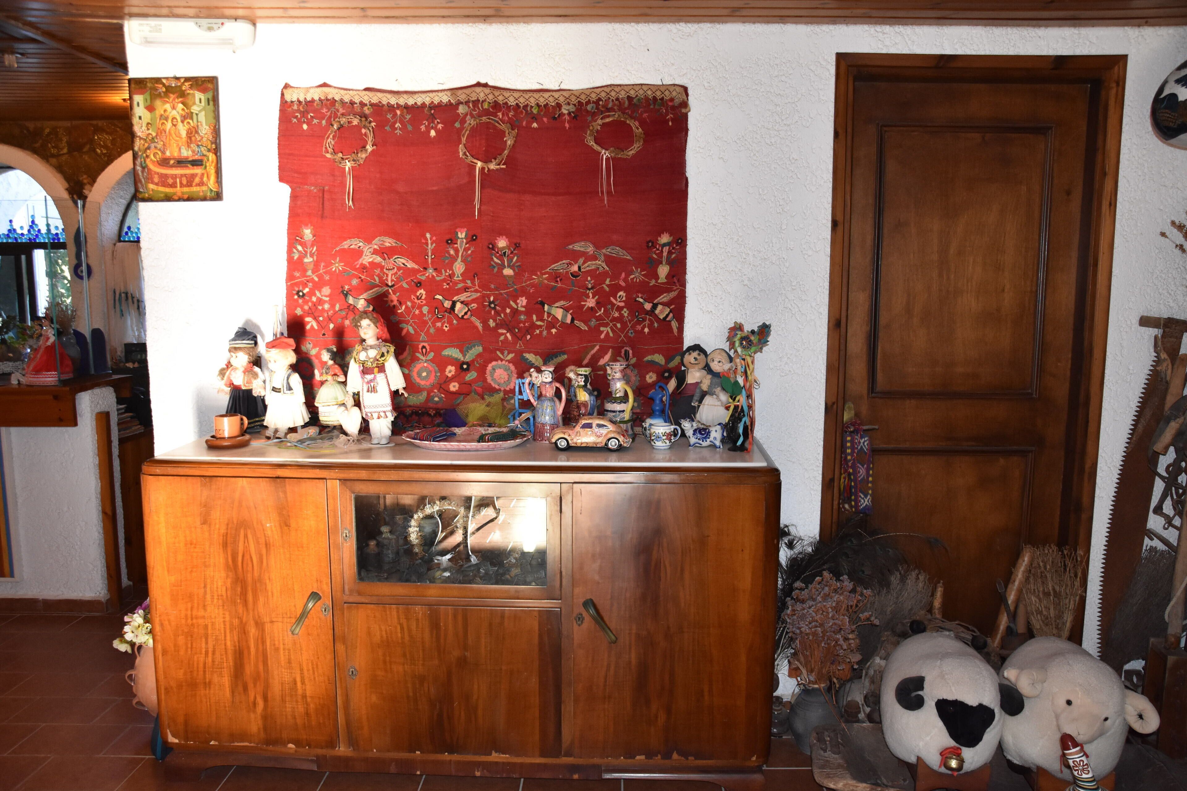 A wooden cabinet with glass doors, decorated with various figurines and a red tapestry with floral patterns.