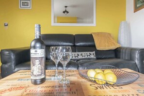 Una botella de vino, dos copas y un bol de limones sobre una mesa con un periódico debajo.