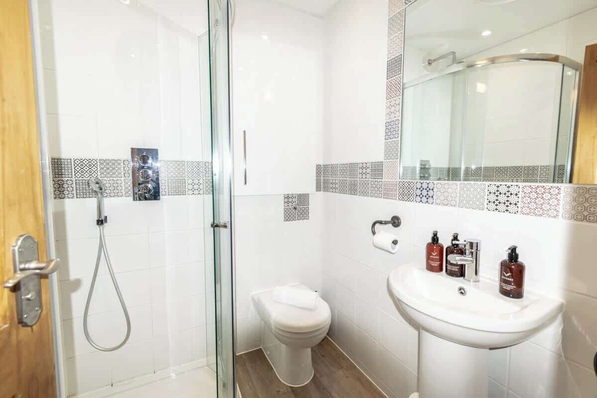 Une salle de bain avec une douche à parois de verre, des toilettes, un lavabo avec des articles de toilette et des carreaux décorés.