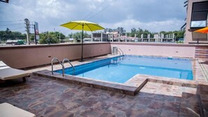 Una piscina en la azotea con agua cristalina, rodeada de baldosas de piedra y equipada con sillones de descanso y un paraguas amarillo.