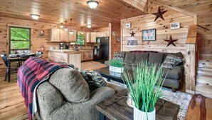 A cozy cabin interior with wooden walls, a dining area, a kitchen, and a living room with a sofa and coffee table. - Spacious Cabin 15 min to Dollywood w/Hot Tub, Game Room, Valley Views (Sevierville)