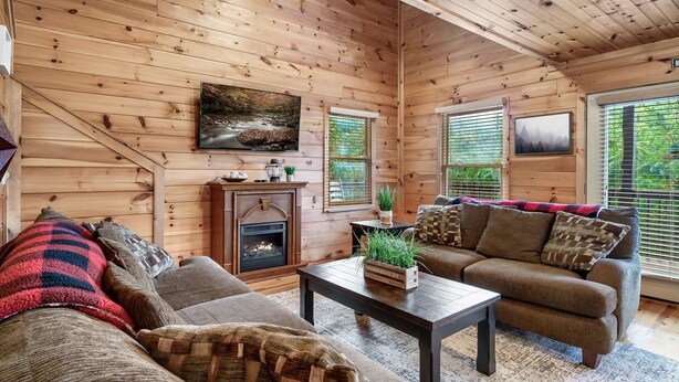 A cozy log cabin interior with a fireplace, wooden walls, a sofa, and a coffee table. - Spacious Cabin 15 min to Dollywood w/Hot Tub, Game Room, Valley Views (Sevierville)