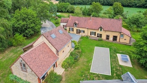 Un'ampia casa con tetto in tegole rosse, immersa nel verde e circondata da campi.