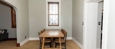 A dining area with a wooden table and chairs, a window with blinds, and a carpeted floor.