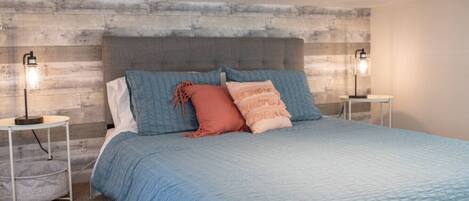 Een slaapkamer met een groot bed, twee nachtkastjes en een hoofdbord tegen een structuurwand.
