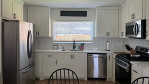 A modern kitchen with white cabinets, stainless steel appliances, a herringbone tile backsplash, and a window with blinds. - Updated Bungalow - Close to town and 30 min from Lubbock! (Brownfield)