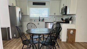 A modern kitchen with white cabinets, a stainless steel refrigerator, a microwave, and a dining area with a round table and four chairs. - Updated Bungalow - Close to town and 30 min from Lubbock! (Brownfield)