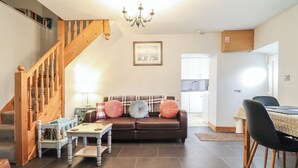 Ein Wohnzimmer mit einem braunen Ledersofa, einer Holztreppe, einem Essbereich mit Tisch und Stühlen sowie einer Küche im Hintergrund.