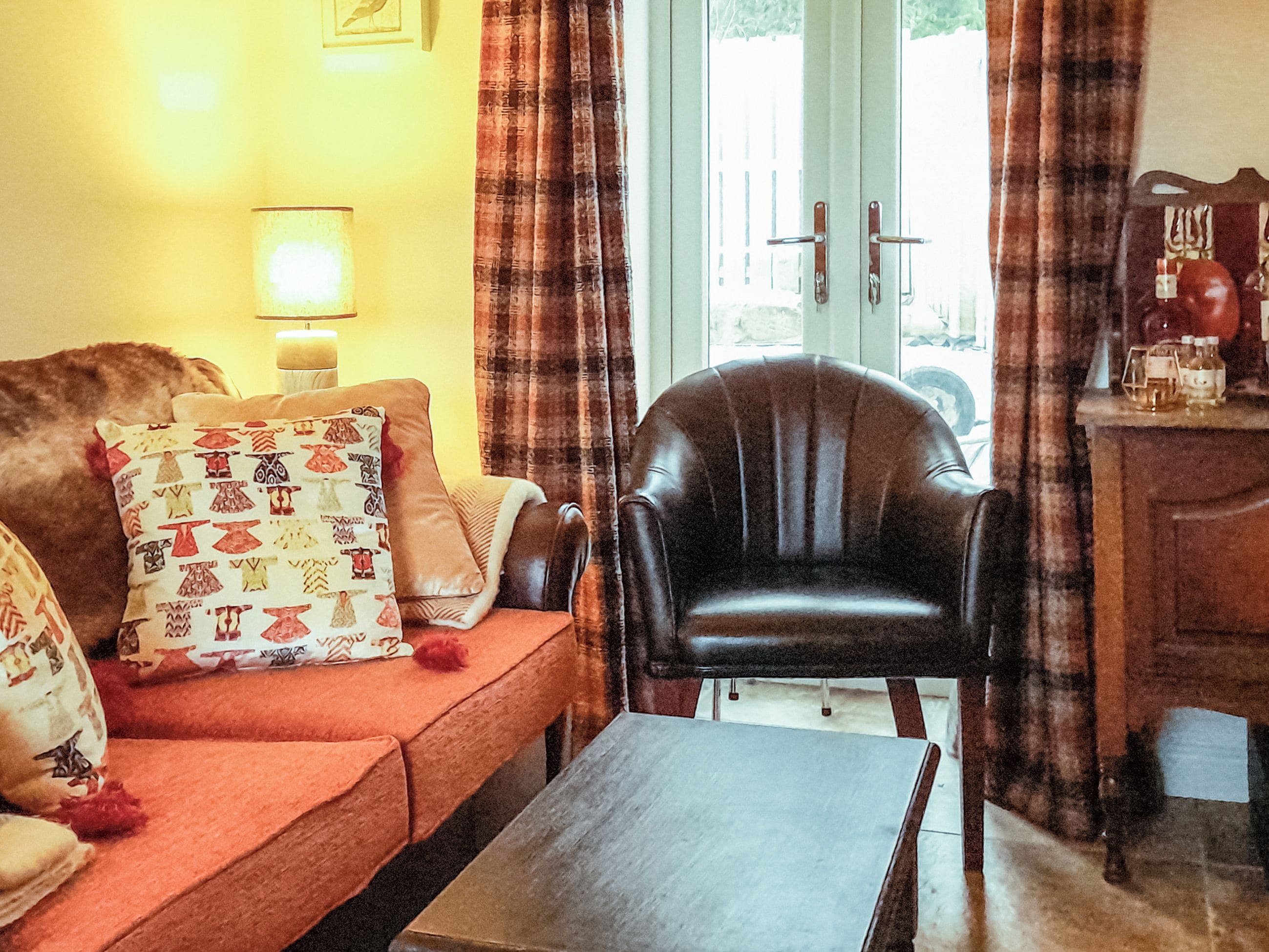 A living room with a brown leather armchair, a red sofa with patterned cushions, and a wooden coffee table.