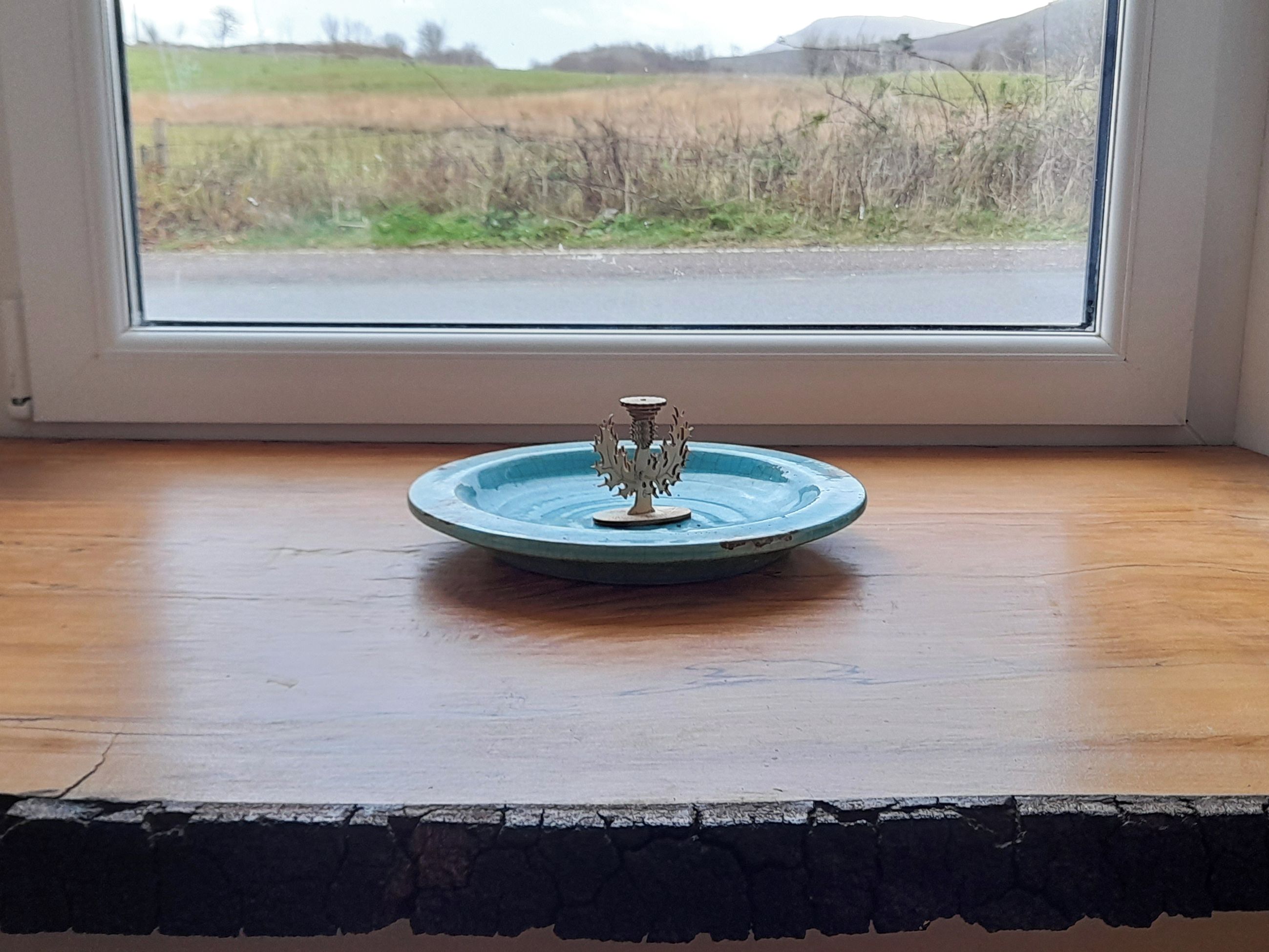 A small blue ceramic dish with a decorative metal stand on a wooden surface by a window.