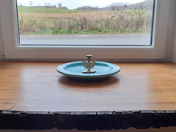 A small blue ceramic dish with a decorative metal stand on a wooden surface by a window.