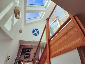 A high-ceilinged room with skylights, a wooden staircase, and a dining area with a blue and white wall decoration.