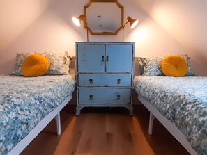 Une chambre avec deux lits, une commode et un miroir au mur.