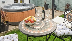 A hot tub with a wooden exterior, a table with a mosaic top, and a bowl of fruit. - 1 bedroom accommodation in Mundesley (Mundesley)