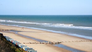 A beach with a long row of colorful beach huts along the shore, a wooden pier extending into the water, and a clear blue sky. - 1 bedroom accommodation in Mundesley (Mundesley)