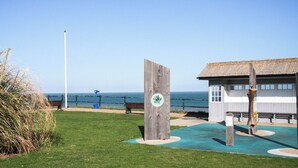 A coastal park with a wooden structure, a bench, and a building with a tiled roof. - 1 bedroom accommodation in Mundesley (Mundesley)
