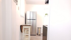 Un couloir étroit avec un réfrigérateur en acier inoxydable, une petite table en bois et une poubelle.