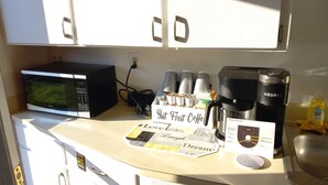 Un comptoir de cuisine avec un four à micro-ondes, une machine à café et une pancarte sur laquelle on peut lire : « Café d’abord ».