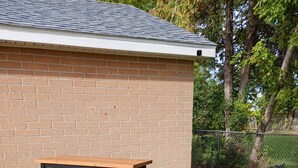 Une table de pique-nique et des bancs sont installés dans un espace verdoyant, avec un mur de briques et une clôture en treillis métallique en arrière-plan.