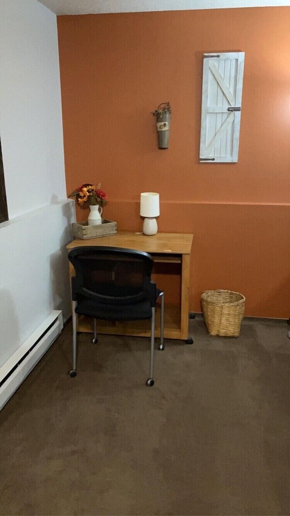 A small room with a desk, chair, lamp, and a decorative item on the wall.