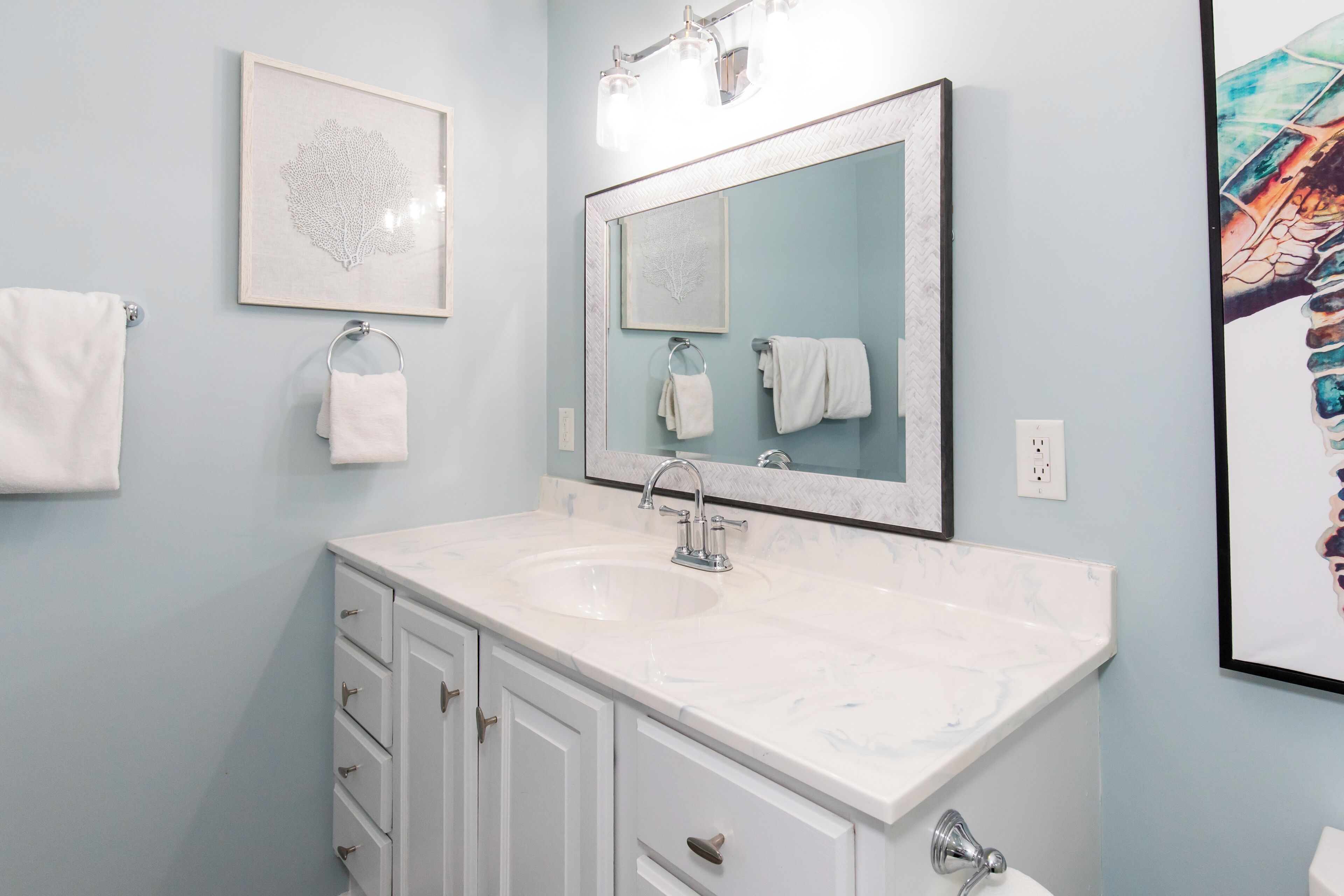 A bathroom with a white vanity, a large mirror, and two framed artworks on the wall.