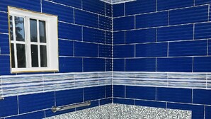 Een badkamer met een wit bad, een raam en blauwe betegelde wanden.