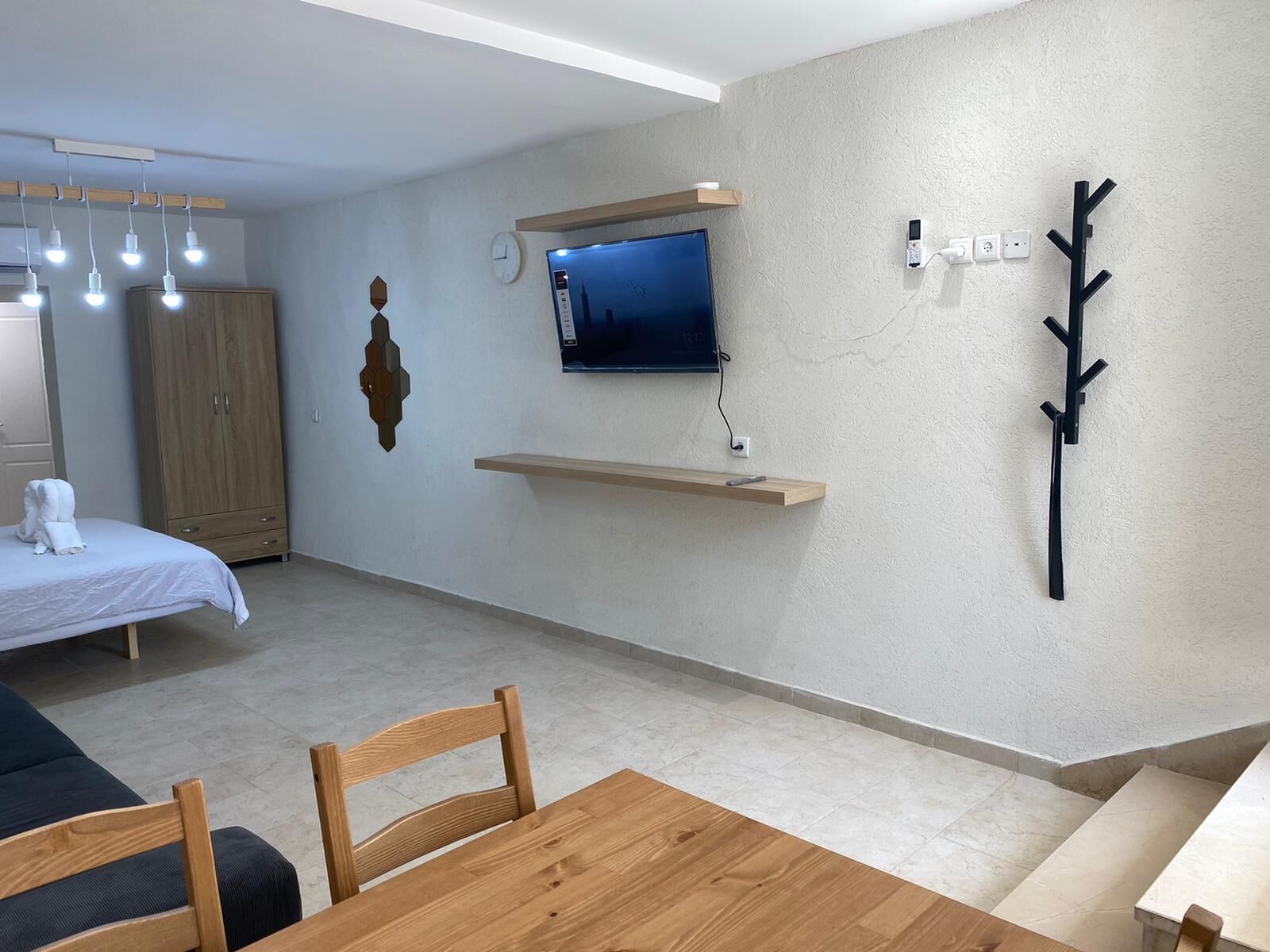 A modern room with a bed, a TV mounted on a wall, a wooden table, and a chair.