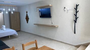 Une chambre moderne avec un lit, un téléviseur fixé au mur, une table en bois et une chaise.