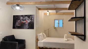 Ett sovrum med en säng, en svart stol, en tavla, en skrivbordslampa och ett fönster.